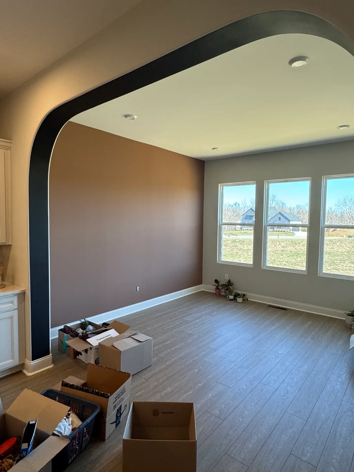 Sunlit room with brown accent wall, large windows, unpacked boxes, and hints of recent exterior house painting. - My Personal Painter Sunlit room with brown accent wall, large windows, unpacked boxes, and hints of recent exterior house painting.