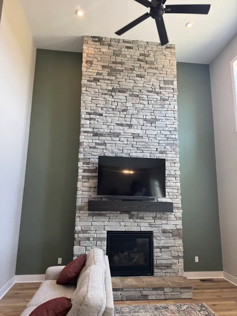 Tall stone fireplace with a mounted TV, black mantel, and light sofa—perfect after your Exterior House Painting project.