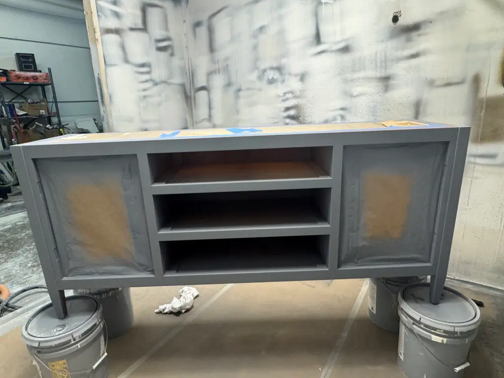 A gray-painted cabinet with open shelves sits on paint cans in a workshop used for exterior house painting projects. - My Personal Painter A gray-painted cabinet with open shelves sits on paint cans in a workshop used for exterior house painting projects.