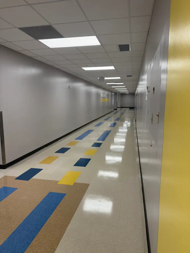 Long, empty school hallway with white walls and colorful rectangular floor tiles in blue, yellow, and brown.