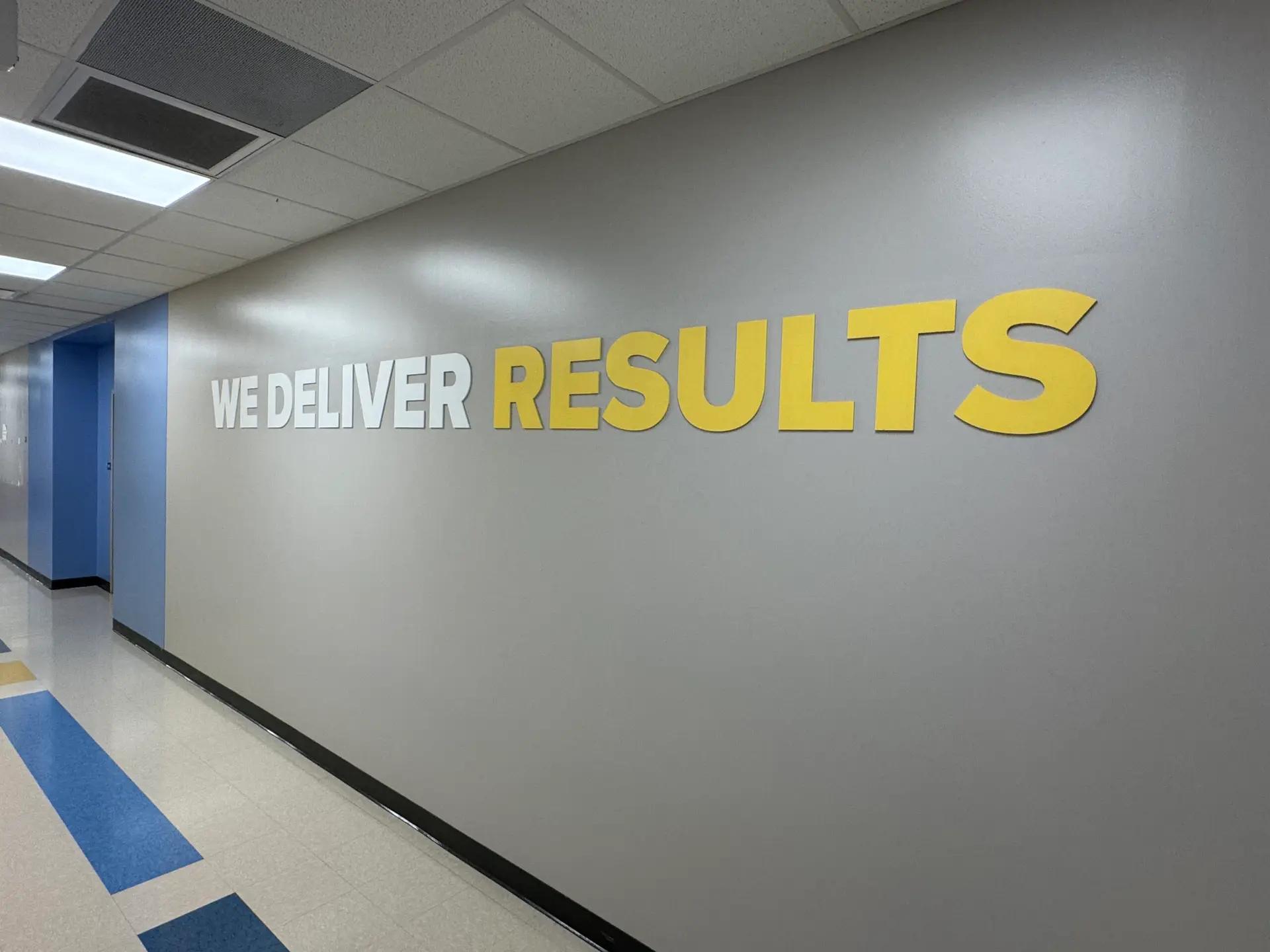 A hallway with the words WE DELIVER RESULTS in large white and yellow letters on a gray wall. - My Personal Painter A hallway with the words WE DELIVER RESULTS in large white and yellow letters on a gray wall.