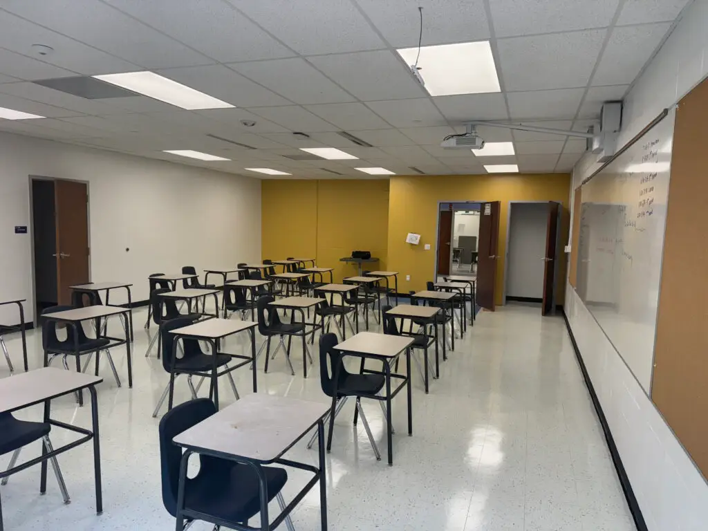 Empty classroom with individual desks and chairs, a whiteboard, and yellow accent wall near the door at the back. - My Personal Painter Empty classroom with individual desks and chairs, a whiteboard, and yellow accent wall near the door at the back.