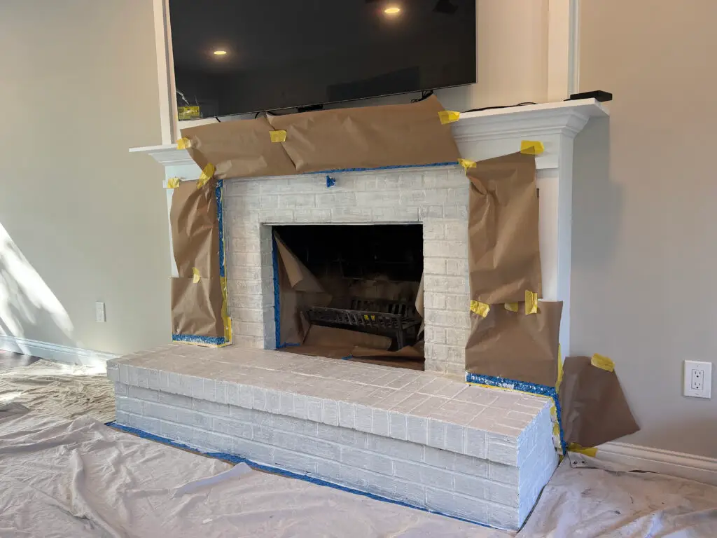 A brick fireplace is covered in painters tape and brown paper, prepared for painting or renovation work.