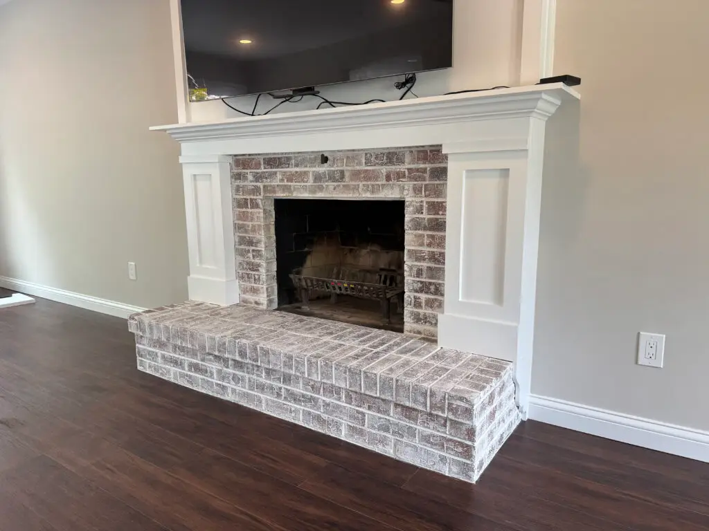 A brick fireplace with a white mantel, a TV mounted above, and dark wood floors in a modern living room.