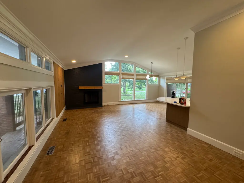 Spacious living room with wood floors, large windows, fireplace, and open kitchen area with pendant lights. - My Personal Painter Living room with smooth, freshly painted walls and wood floors after drywall repair