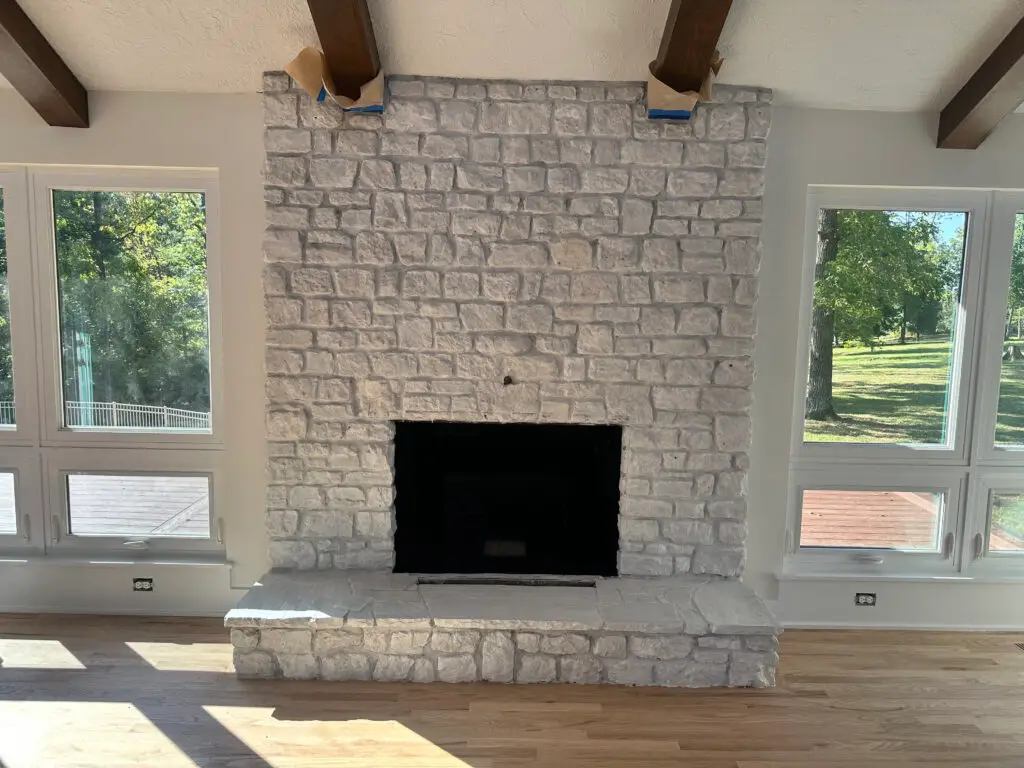A large stone fireplace with a black firebox, flanked by tall windows letting in natural light. - My Personal Painter A large stone fireplace with a black firebox, flanked by tall windows letting in natural light.