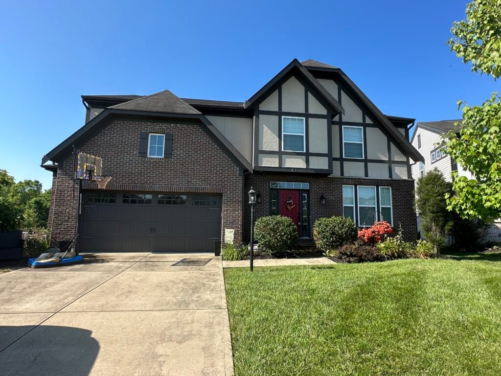 Two-story house with brick and Tudor-style exterior, red front door, and green lawn under a clear blue sky. - My Personal Painter - My Personal Painter Two-story brick home exterior freshly painted by My Personal Painter in Northern Kentucky