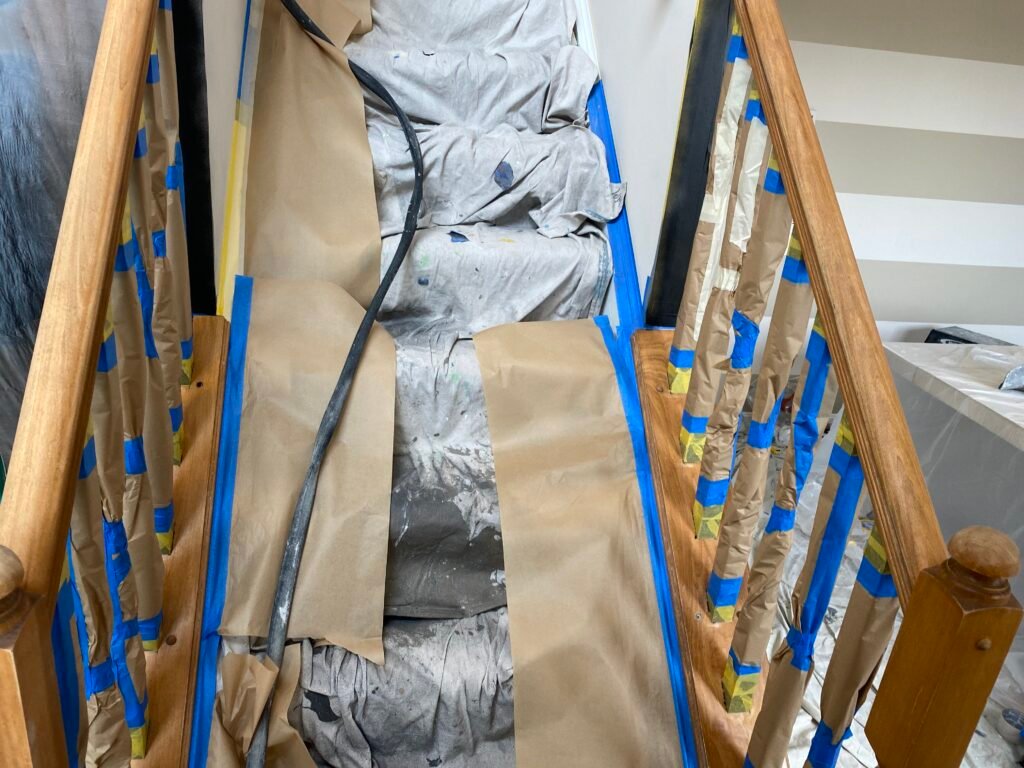 A staircase covered with protective paper, fabric, and blue tape, prepared for painting or renovation work.