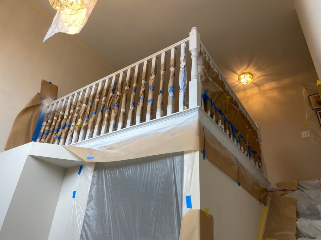 A staircase and railing covered with tape and plastic, prepared for painting or renovation work. - My Personal Painter A staircase and railing covered with tape and plastic, prepared for painting or renovation work.
