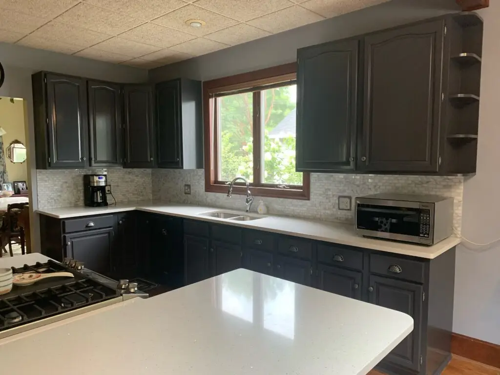 Modern kitchen with dark cabinets, white countertops, a microwave, coffee maker, and a large window above the sink.