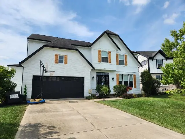 Two-story white house with black roof, wooden shutters, driveway, garage, and a basketball hoop by the garage. - My Personal Painter - My Personal Painter Two-story white house with a freshly painted exterior and black trim