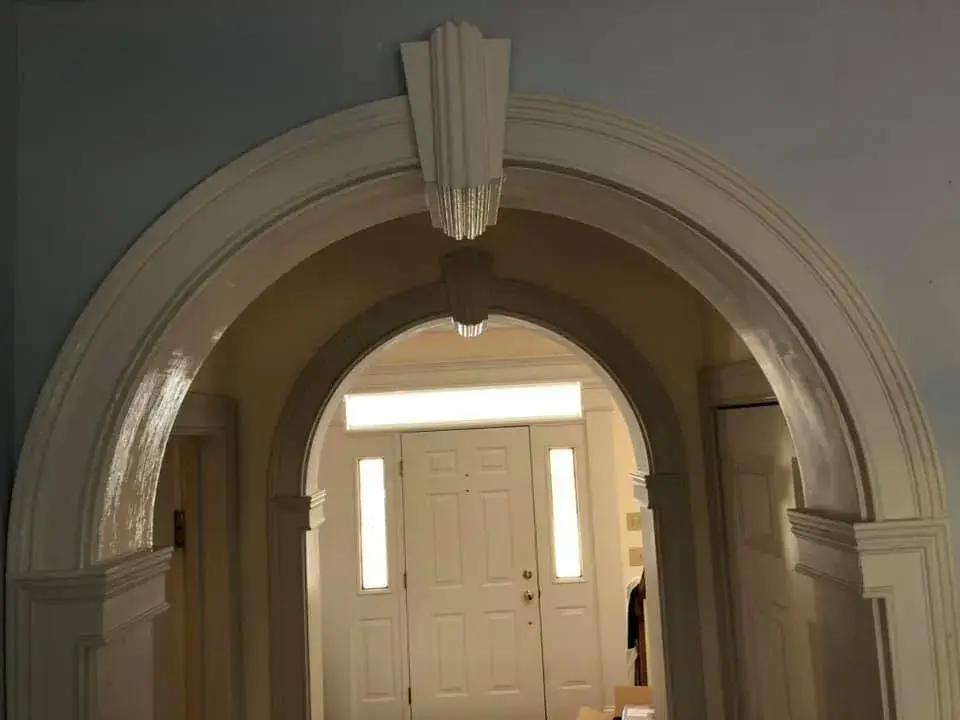 A double-arched doorway with Art Deco-style architectural details leading to a front door. - My Personal Painter - My Personal Painter In progress: arched trim, doorway and window niche painted