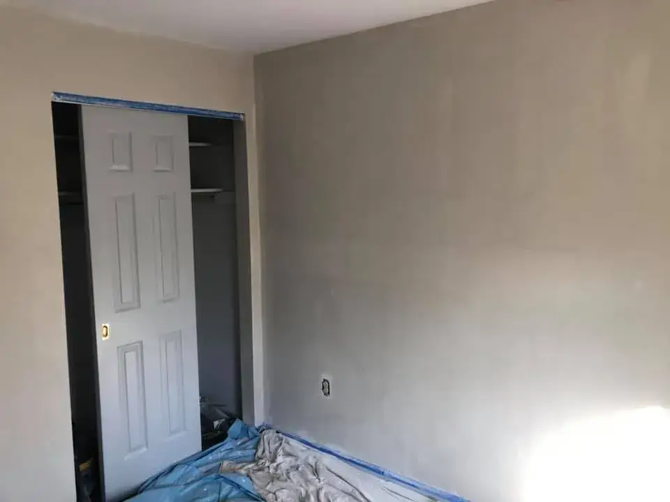 A room interior with freshly painted gray walls, a partial closet door, and a drop cloth on the floor. - My Personal Painter - My Personal Painter After: bedroom walls repaired and painted
