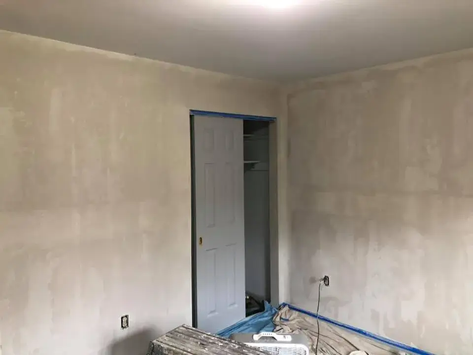 A room under renovation with patch-filled drywall, a closet door, and painters tape on the baseboards. - My Personal Painter - My Personal Painter In progress: bedroom walls repaired and painted