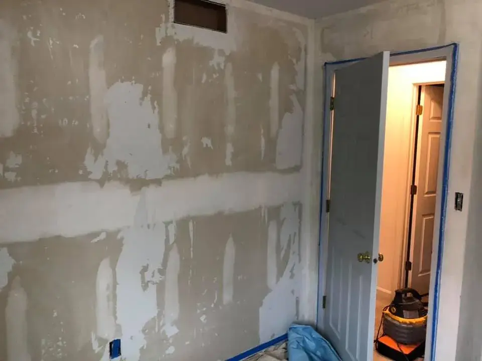 A room under renovation with drywall patches on the walls and an open doorway leading to another room. - My Personal Painter - My Personal Painter In progress: bedroom walls repaired and painted