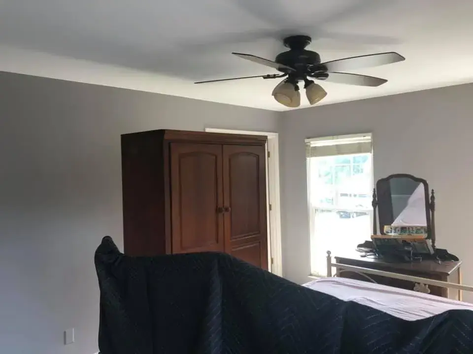 A bedroom featuring a tall wooden wardrobe, a window, a vanity with a mirror, and a bed covered by a quilted blanket. - My Personal Painter - My Personal Painter After: bedrooms with wallpaper borders painted gray