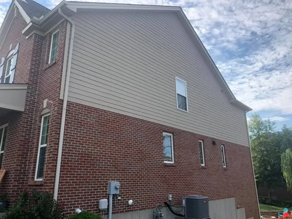 The side of a two-story house featuring red brick on the bottom level and tan siding on the upper level. - My Personal Painter - My Personal Painter After: brick and tan siding house exterior painted