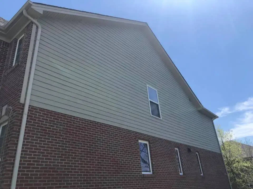 A house exterior featuring light green horizontal siding above a red brick base with several windows. - My Personal Painter - My Personal Painter After: brick and tan siding house exterior painted