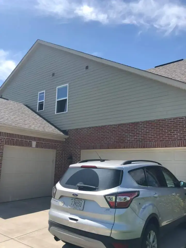 Silver SUV parked in the driveway of a two-story home with a brick and light green siding exterior. - My Personal Painter - My Personal Painter After: brick and tan siding house exterior painted