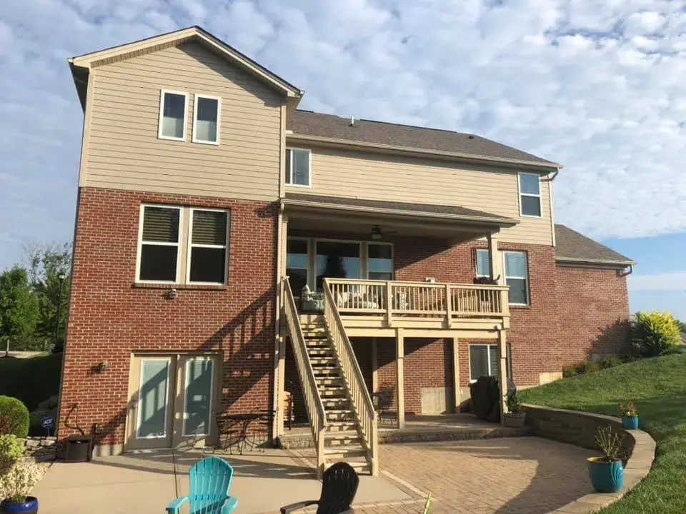 Two-story brick and siding house with a raised wooden deck and stairs leading to a backyard patio. - My Personal Painter - My Personal Painter After: brick and tan siding house exterior painted