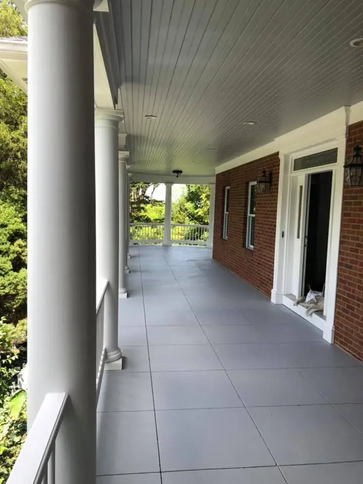 Covered porch with white columns and grey tiled flooring along a brick house wall. - My Personal Painter - My Personal Painter After: brick home: round wraparound porch and rear deck with brick columns