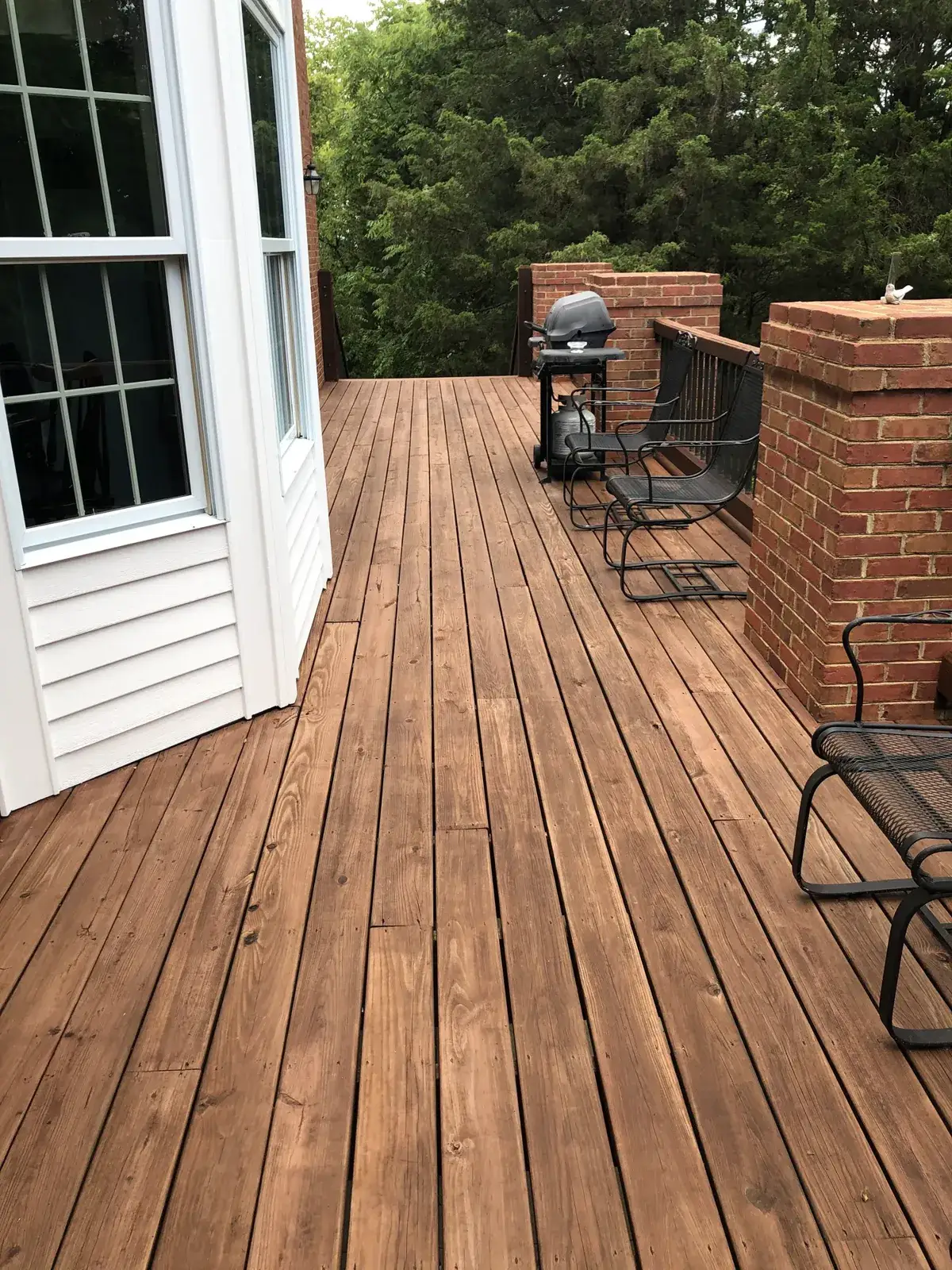 A wooden deck with a grill and outdoor chairs outside a house. - My Personal Painter - My Personal Painter After: brick home: round wraparound porch and rear deck with brick columns