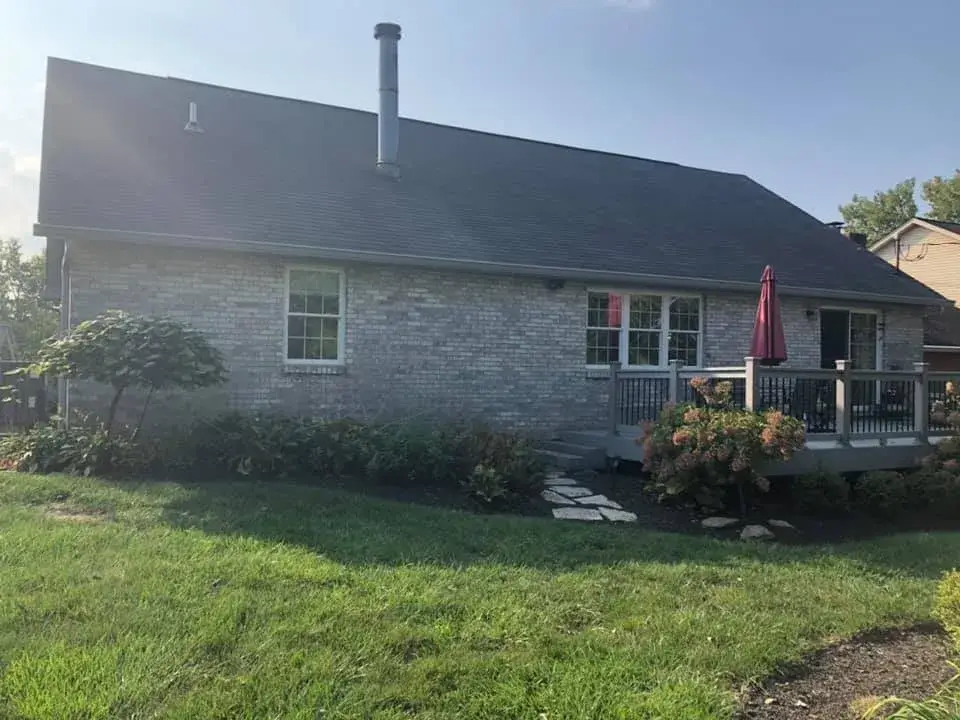 A gray brick house with a dark shingle roof, a metal chimney, and a raised wooden deck in the backyard. - My Personal Painter - My Personal Painter Before: brick ranch exterior painted light gray