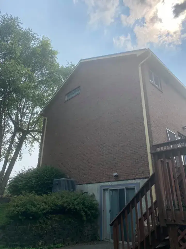 A two-story brick house with a wooden deck and a small window near the roofline. - My Personal Painter - My Personal Painter In progress: brick two-story house: siding and trim painted