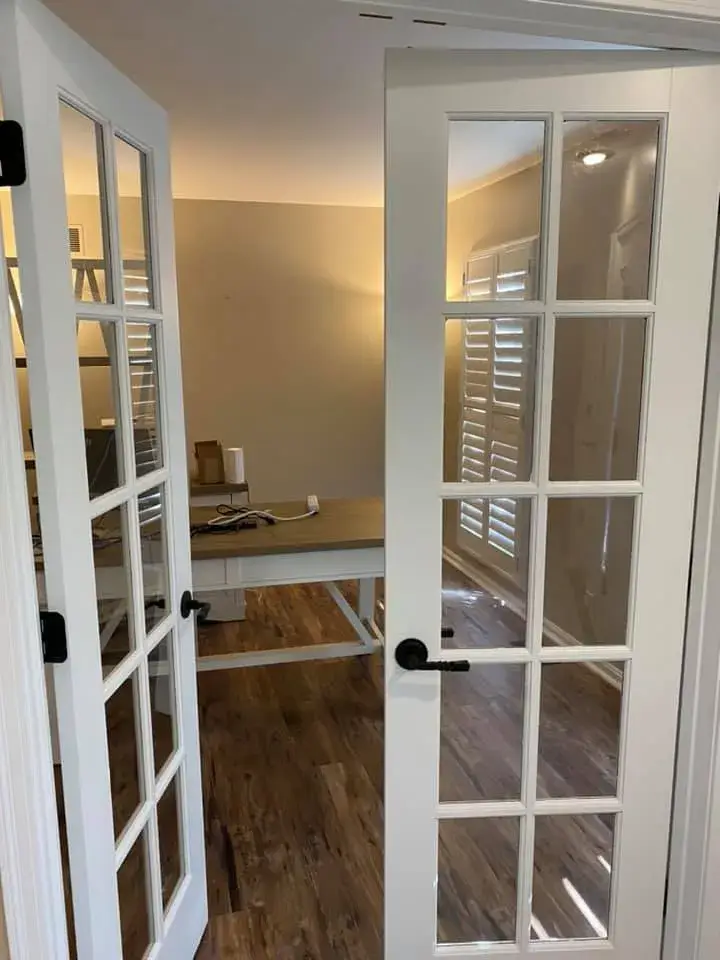 Open white French doors leading into an office with a desk and wood-look flooring. - My Personal Painter - My Personal Painter After: ceiling beams painted black, brick fireplace whitewashed, other rooms