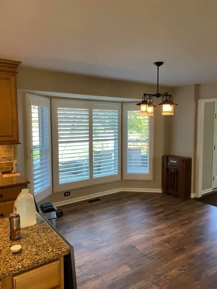 Dining area with a bay window, wood flooring, and a hanging pendant light. - My Personal Painter - My Personal Painter After: ceiling beams painted black, brick fireplace whitewashed, other rooms