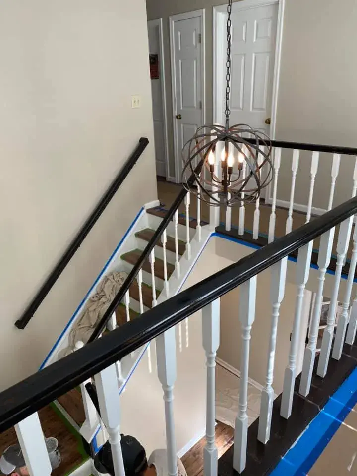 A staircase with a black handrail and white spindles, featuring a metal orb chandelier hanging above the landing. - My Personal Painter - My Personal Painter In progress: ceiling beams painted black, brick fireplace whitewashed, other rooms