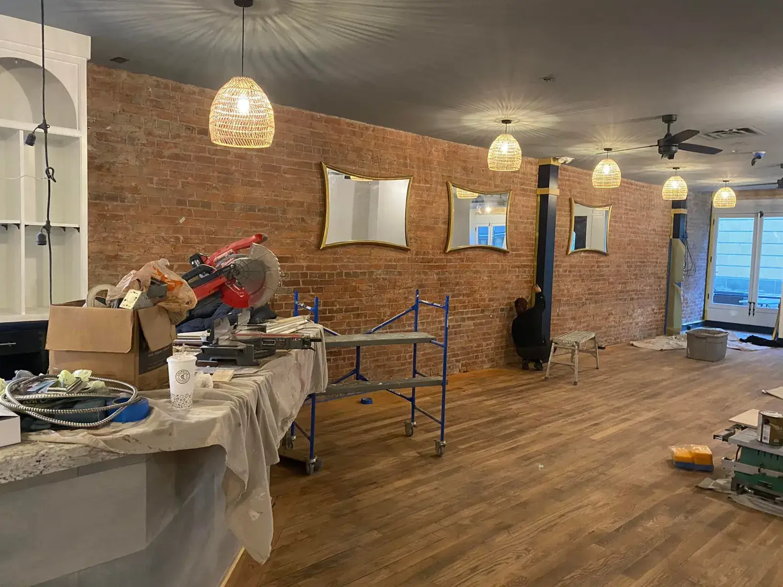 A person works on a brick wall in a commercial space under renovation with tools and scaffolding. - My Personal Painter - My Personal Painter In progress: commercial space: exposed brick to whitewash