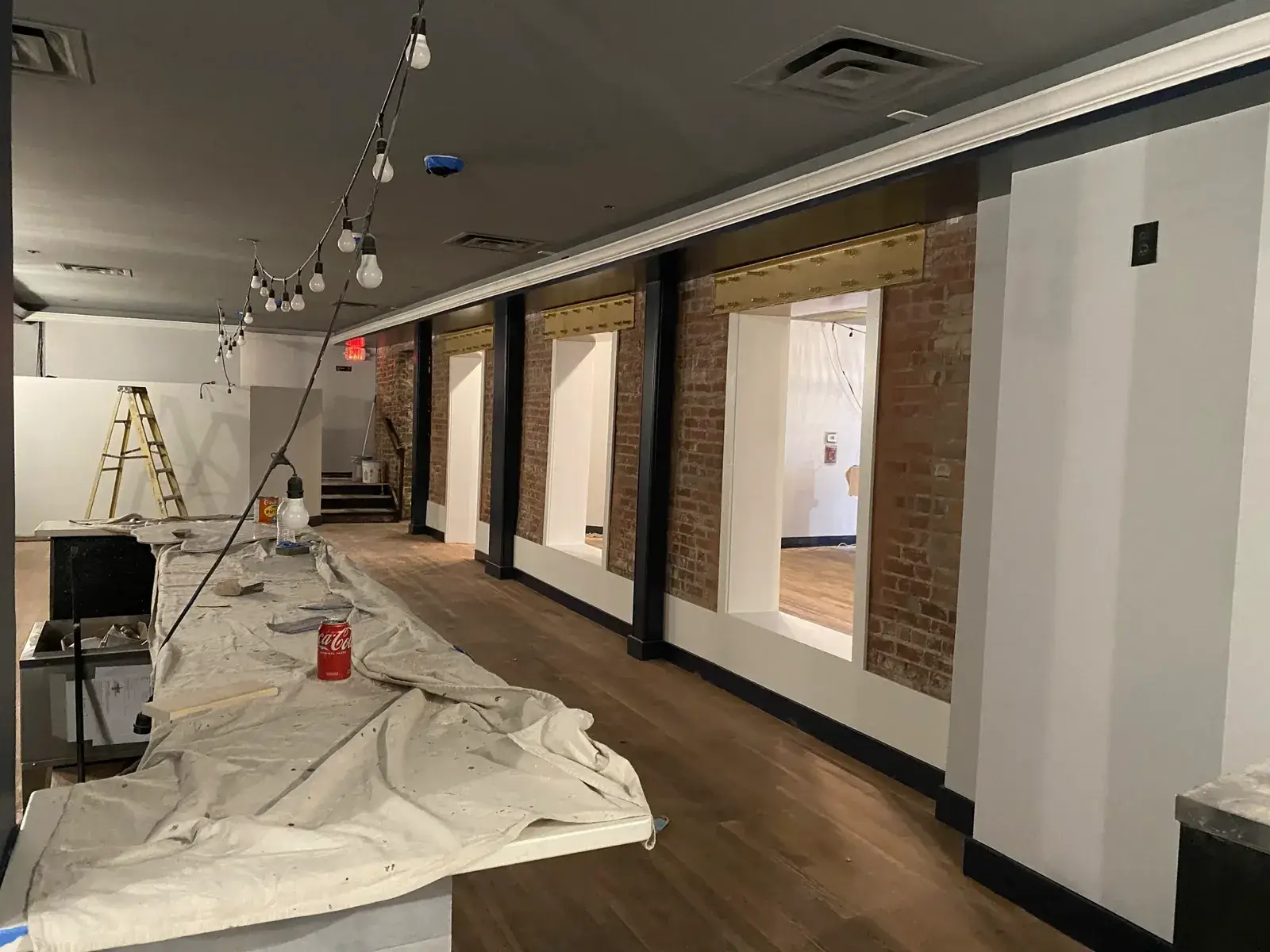 A room under renovation with a long table covered in a drop cloth and three wall openings revealing brick trim. - My Personal Painter - My Personal Painter In progress: commercial space: exposed brick to whitewash