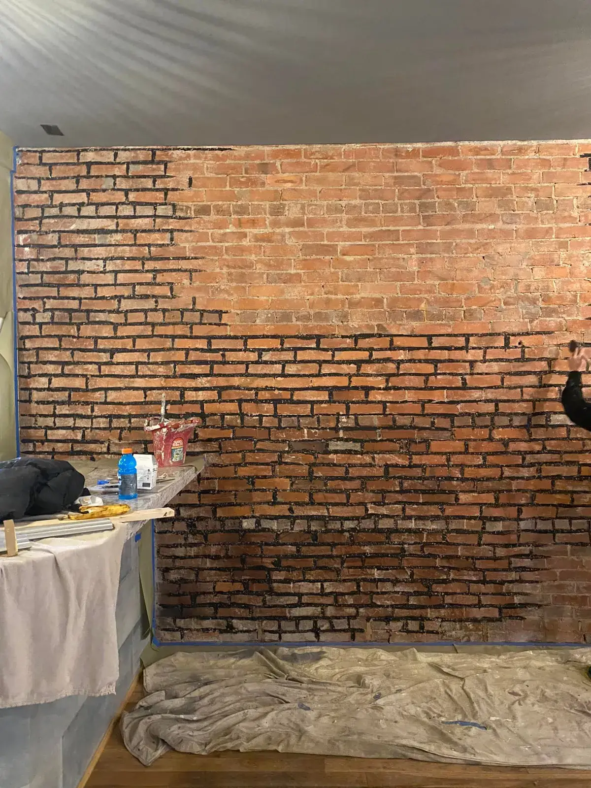 A person paints black grout lines onto a brick wall. - My Personal Painter - My Personal Painter In progress: commercial space: exposed brick to whitewash