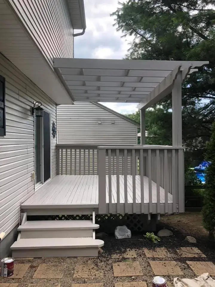 A freshly painted light gray wooden deck with a matching pergola attached to the side of a house. - My Personal Painter - My Personal Painter After: deck and pergola painted gray