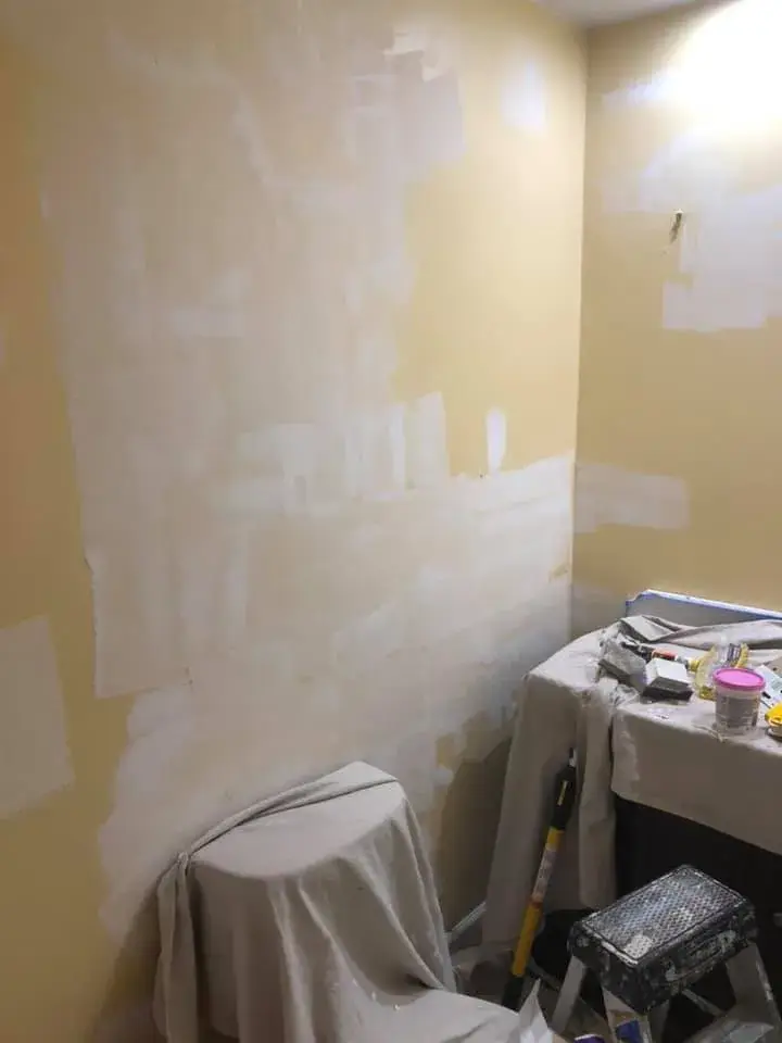 A wall with patches of fresh spackle, with drop cloths covering a toilet and vanity. - My Personal Painter - My Personal Painter In progress: half bath repainted from yellow to blue-gray