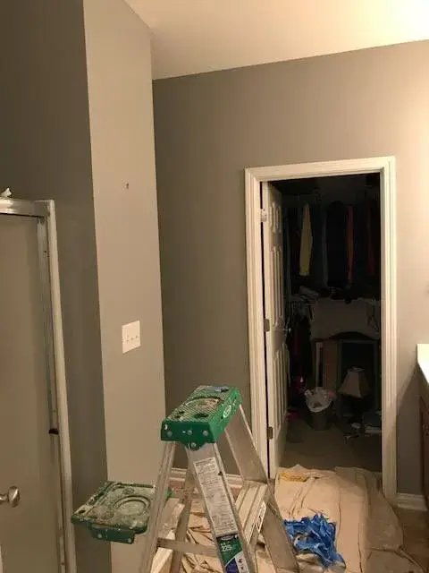 A green step ladder standing on a drop cloth in a room with grey walls and an open walk-in closet. - My Personal Painter - My Personal Painter In progress: hallway, bedrooms, closet and bathroom painted