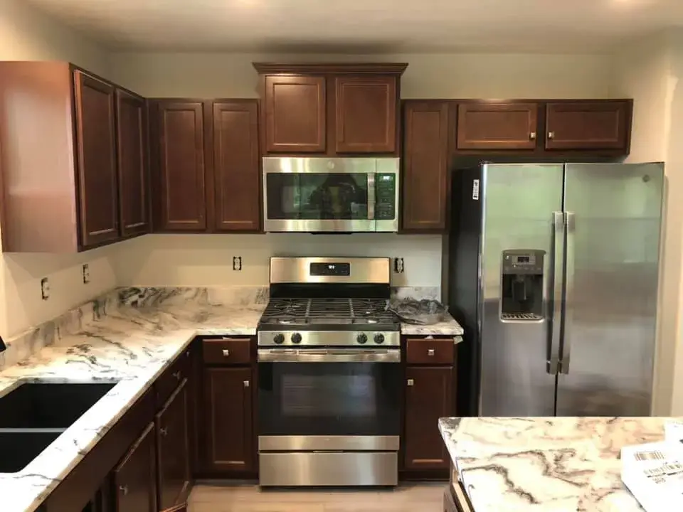 Kitchen with dark wood cabinets, stainless steel appliances, and marbled countertops. - My Personal Painter - My Personal Painter Before: kitchen cherry cabinets painted black