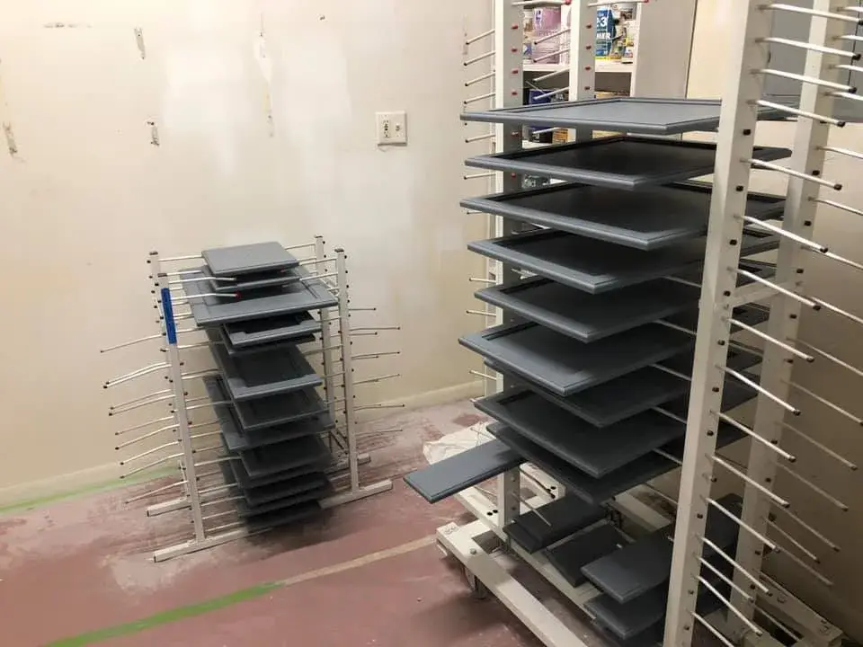 Two metal drying racks holding stacks of painted grey cabinet doors. - My Personal Painter - My Personal Painter In progress: kitchen cherry cabinets painted black