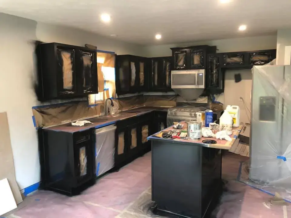 Kitchen cabinets being spray-painted black with protective plastic covering countertops and appliances. - My Personal Painter - My Personal Painter In progress: kitchen cherry cabinets painted black