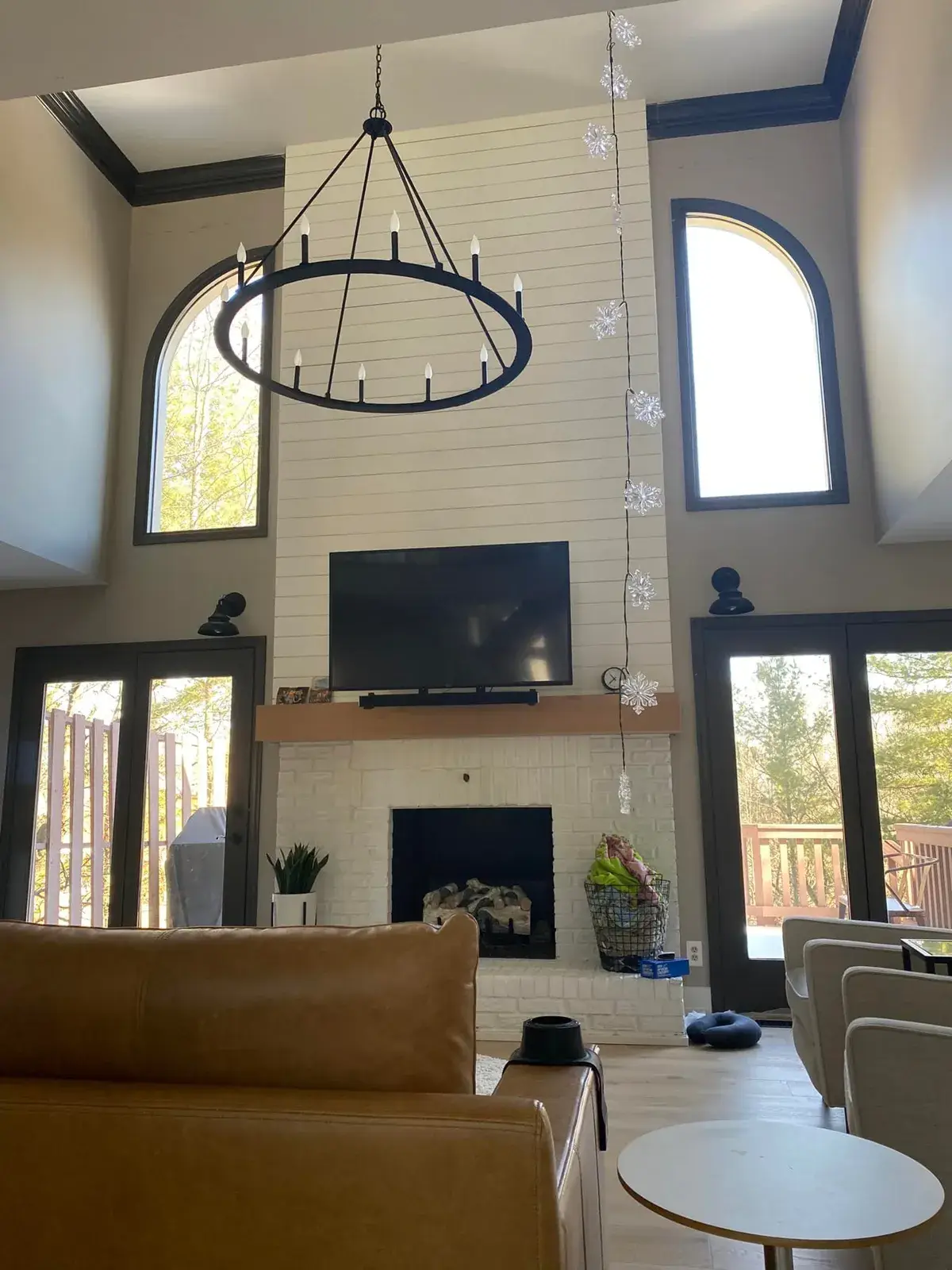 A living room with a white brick fireplace, a mounted television, a large circular chandelier, and arched windows. - My Personal Painter - My Personal Painter After: kitchen cherry cabinets to white with a green island, two-story great room, dining room and foyer