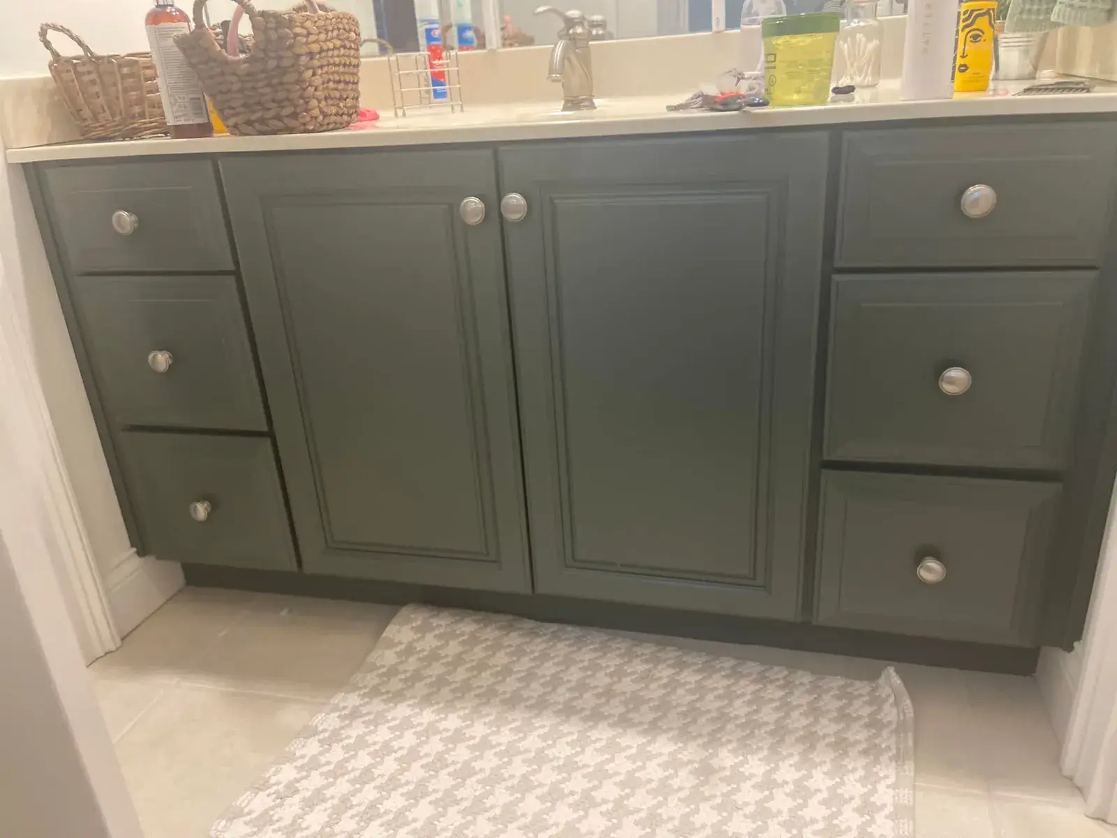 Dark green bathroom vanity with silver knobs and a white countertop holding various toiletries. - My Personal Painter - My Personal Painter After: kitchen cherry cabinets to white with a green island, two-story great room, dining room and foyer