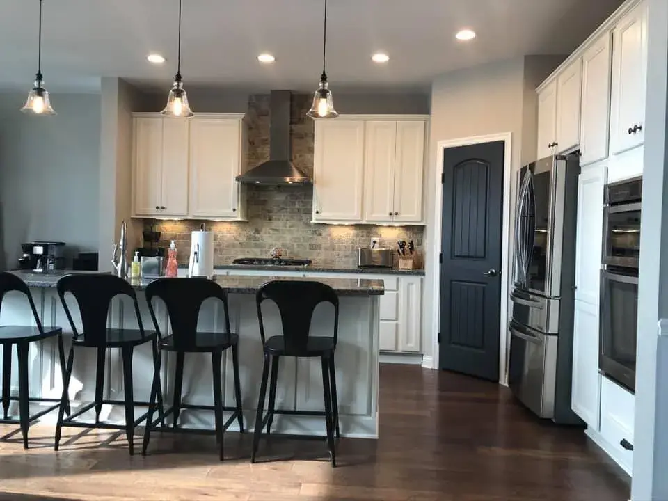 Modern kitchen with white cabinets, a stone backsplash, a stainless steel oven, and four black stools at a kitchen island. - My Personal Painter - My Personal Painter After: kitchen dark cabinets painted white