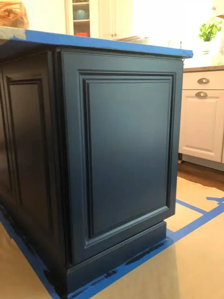 A kitchen island with dark blue paneled cabinets, partially covered in blue painters tape. - My Personal Painter - My Personal Painter In progress: kitchen island painted navy