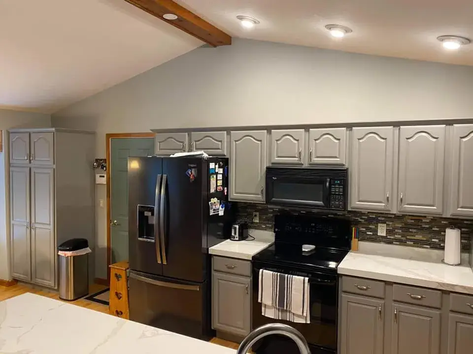 Kitchen with grey cabinets, white countertops, and black appliances. - My Personal Painter - My Personal Painter After: kitchen oak cabinets painted gray, vaulted ceiling with beam