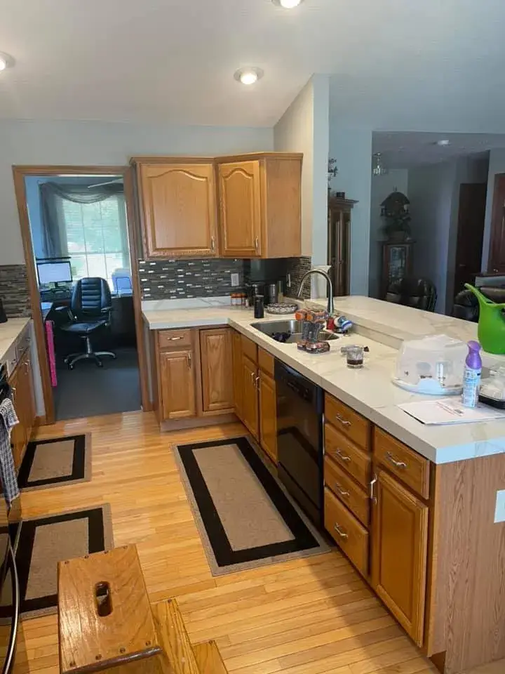 Kitchen with wood cabinets, light countertops, and a view into a home office. - My Personal Painter - My Personal Painter Before: kitchen oak cabinets painted gray, vaulted ceiling with beam