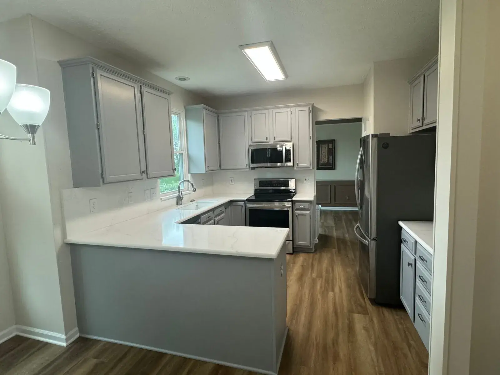 U-shaped kitchen with grey cabinets, white countertops, stainless steel appliances, and wood-look flooring. - My Personal Painter - My Personal Painter After: kitchen wood cabinets painted gray