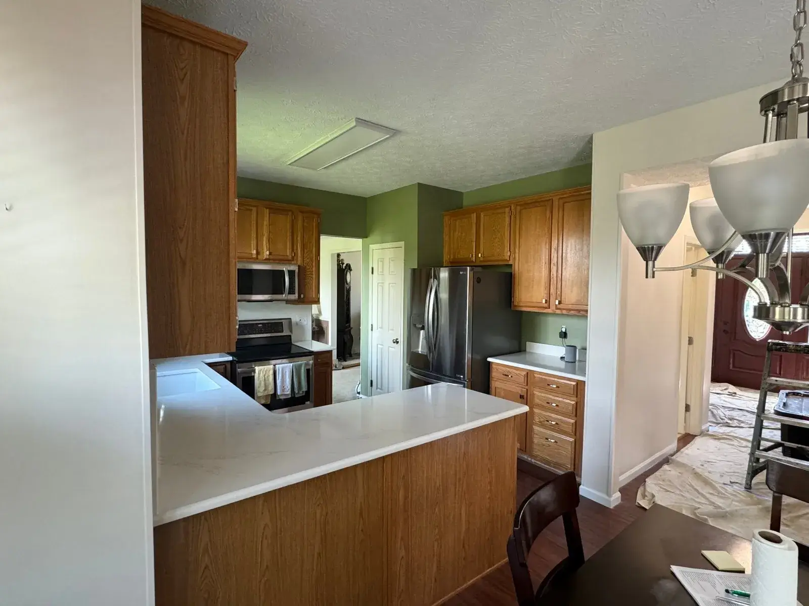 A kitchen with wood cabinets, stainless steel appliances, and a white countertop peninsula. - My Personal Painter - My Personal Painter Before: kitchen wood cabinets painted gray
