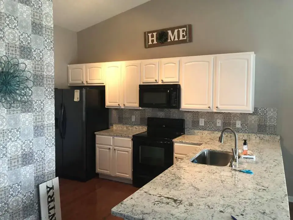 After: kitchen wood cabinets painted white (patterned tile wall, HOME sign)
