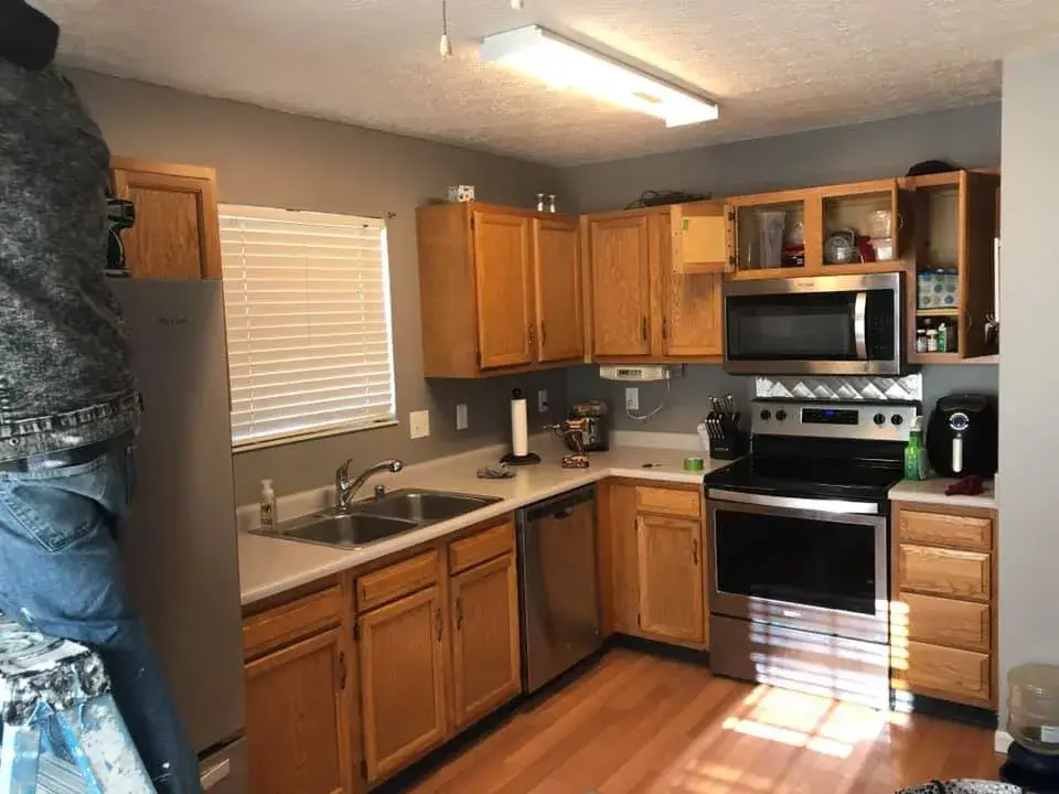 Before: kitchen wood cabinets painted white (patterned tile wall, HOME sign)